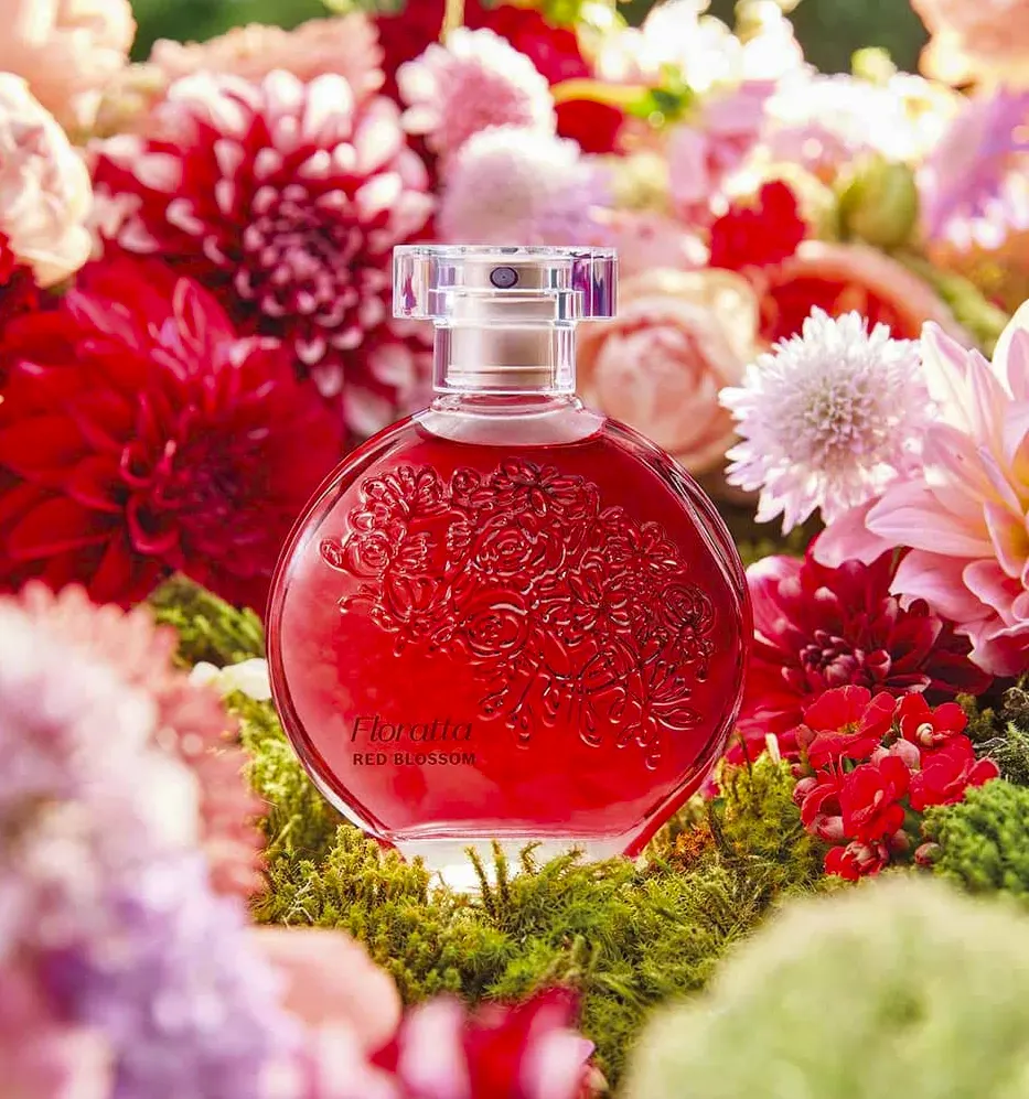 Frasco do perfume Floratta Red da Boticário sobre superfície clara, com fundo floral e iluminação suave que destaca seu design feminino.