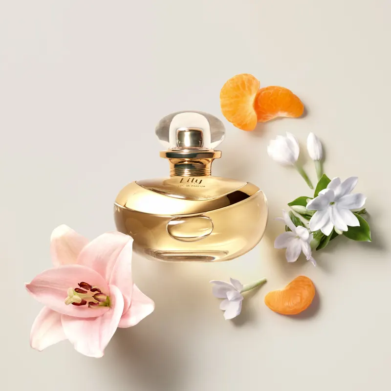Frasco do perfume Lily Eau de Parfum da Boticário sobre superfície clara com flores ao redor, iluminado suavemente para destacar seu design sofisticado.