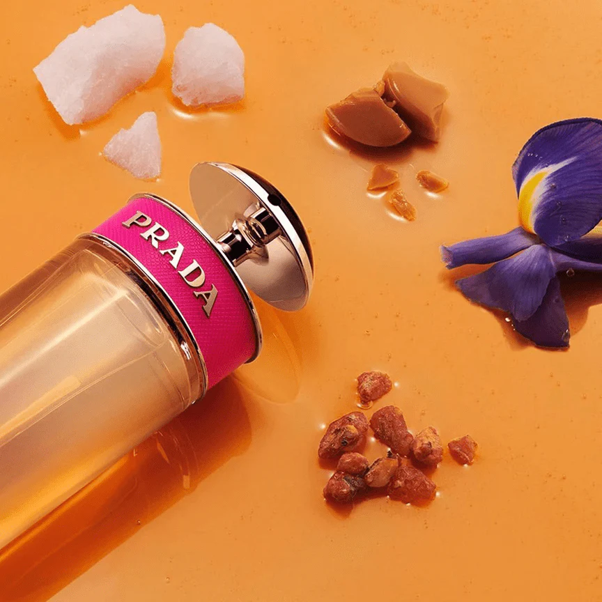 Frasco vibrante do perfume Prada Candy em cenário elegante com elementos que evocam caramelo, baunilha e notas atalcadas, sobre fundo suave e iluminado.