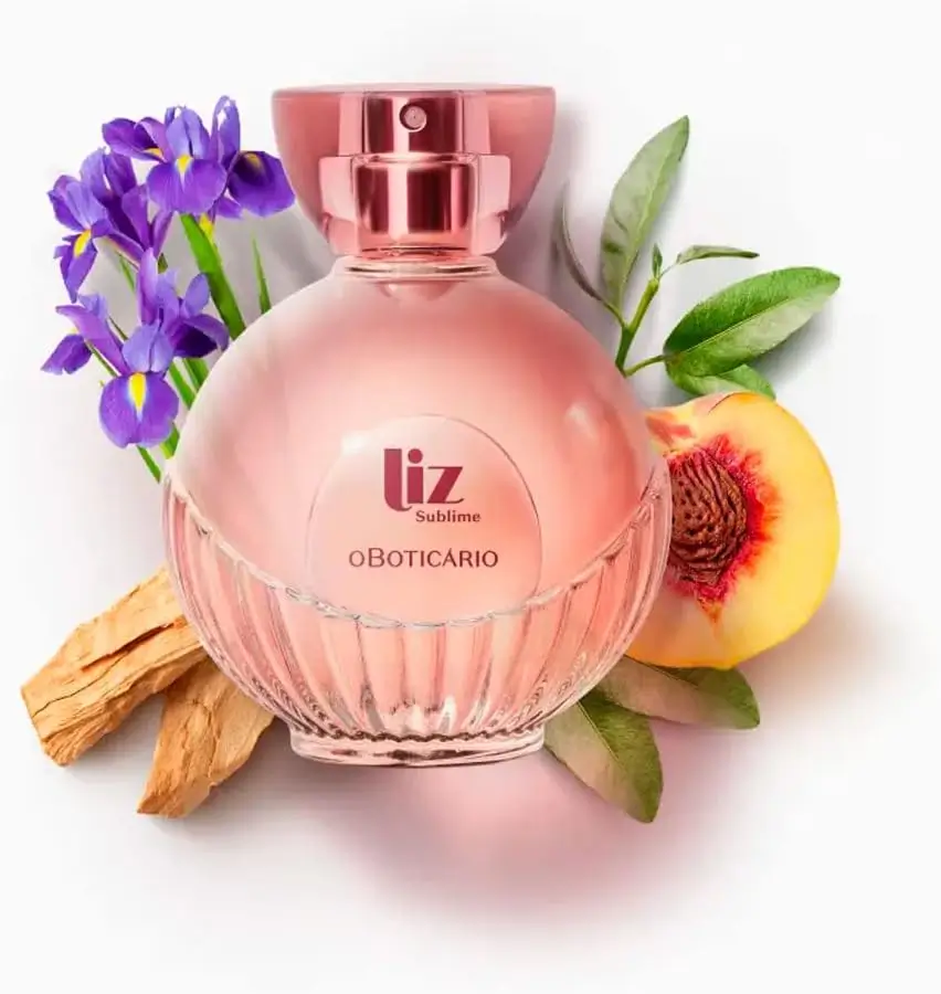 “Perfume Liz Sublime o Boticário em frasco rosé, cercado por flores roxas, pêssego e madeira, destacando notas florais, frutadas e cremosas.”