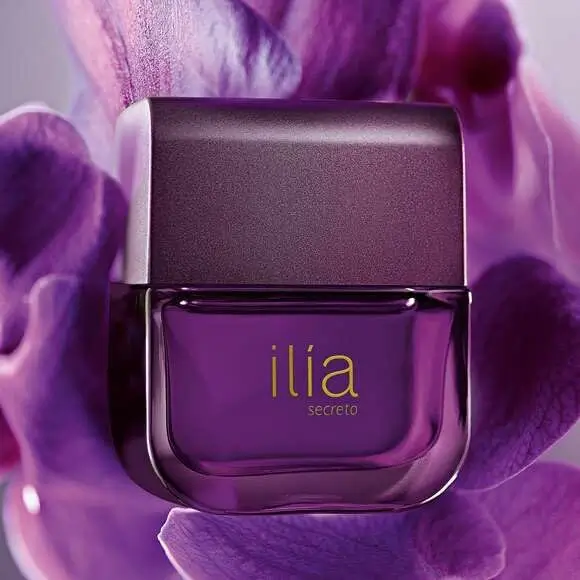 Frasco roxo do perfume Ilía Secreto da Natura sobre fundo floral em tons violeta