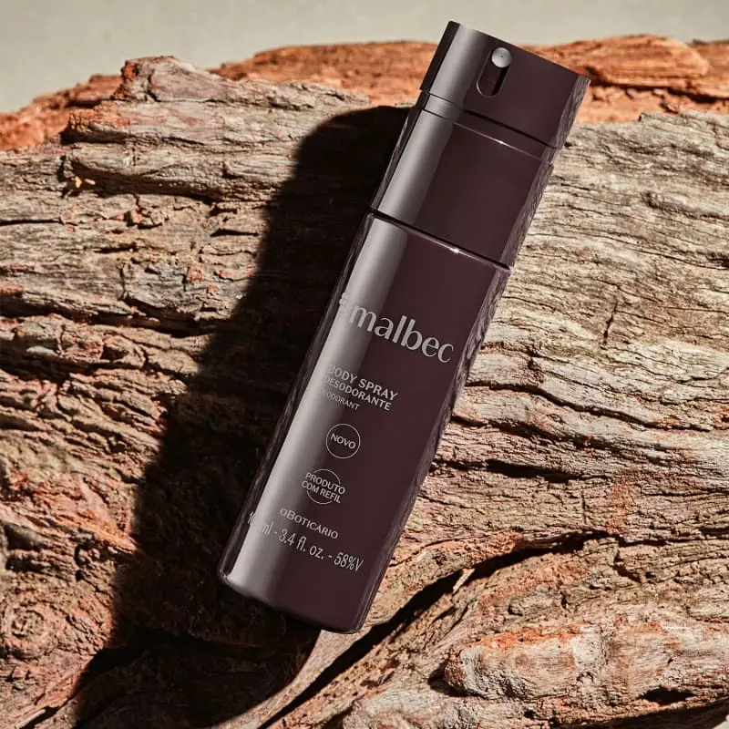 Malbec versões com destaque para o body spray Malbec tradicional de O Boticário sobre fundo amadeirado.